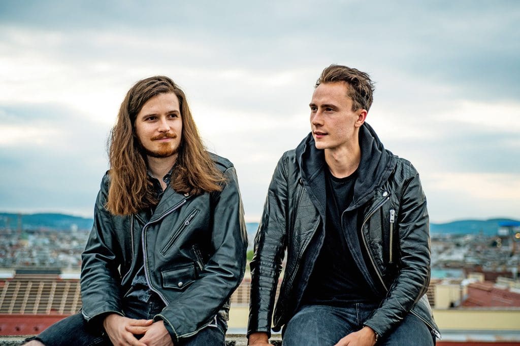 Die Band Krawall in Lederjacken vor dem Panorama-Blick auf eine Stadt. Ihre Blicke gehen an der Kamera vorbei.