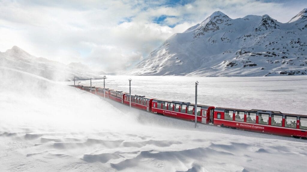 Roter Zug Bernina Express fährt durch ein schneebedecktes Tal beim Lago Bianco in der Schweiz