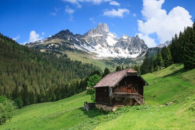 Almhütte auf einer Wiese vor Bergen und blauem Himmel