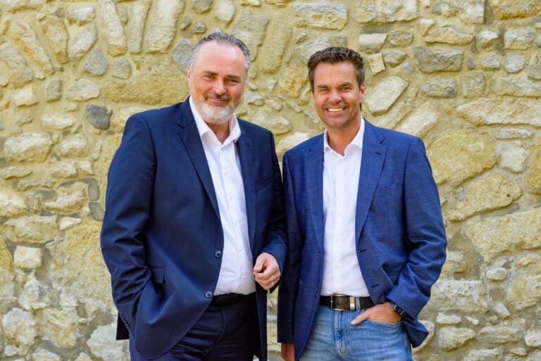 Landeshauptmann Hans Peter Doskozil und Burgenland Tourismus-Geschäftsführer Didi Tunkel vor einer braunen Steinwand