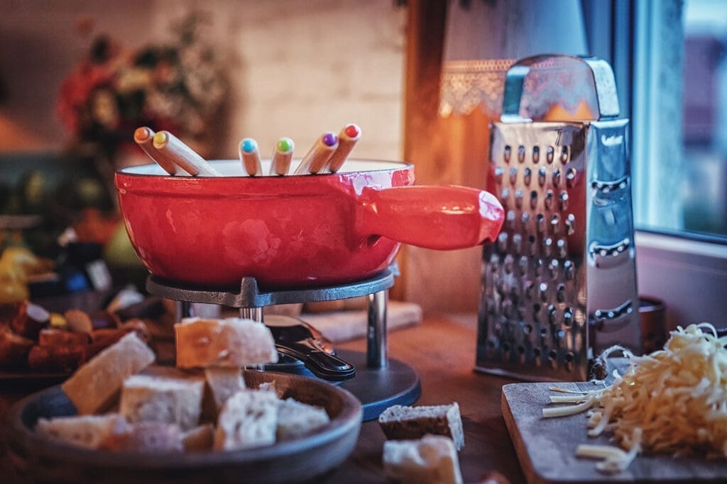 Raclette oder Fondue: Hier Fondue in rotem Topf neben Reibeform.