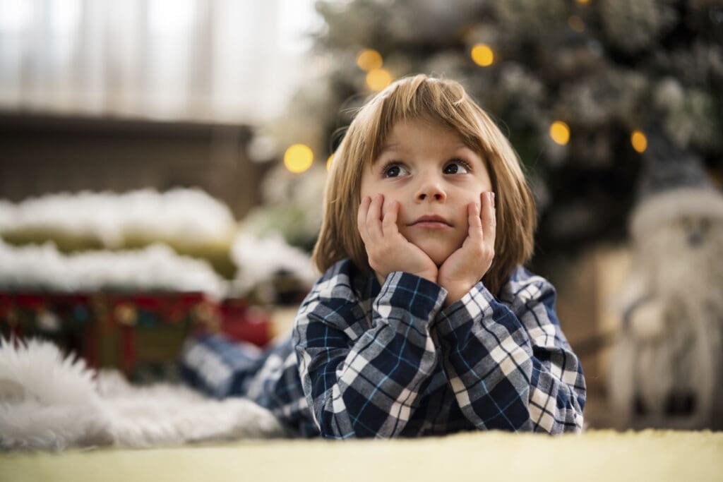 Bub sitzt neben dem Christbaum und denkt nach