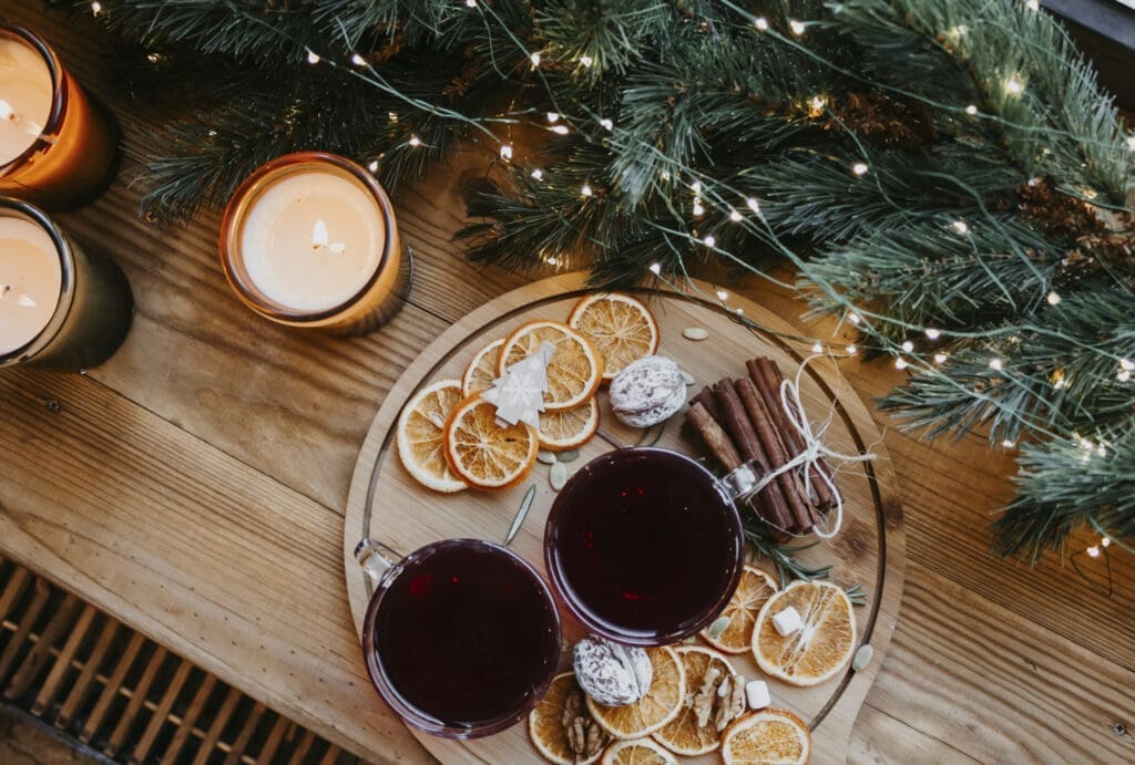 Weihnachtsdeko am Tisch: Kerzen, Tannenzweige, Lichterketten, Orangenscheiben, Nüsse, Tee, Zimtstangen. Das Licht ist warm, der Tisch aus Holz.