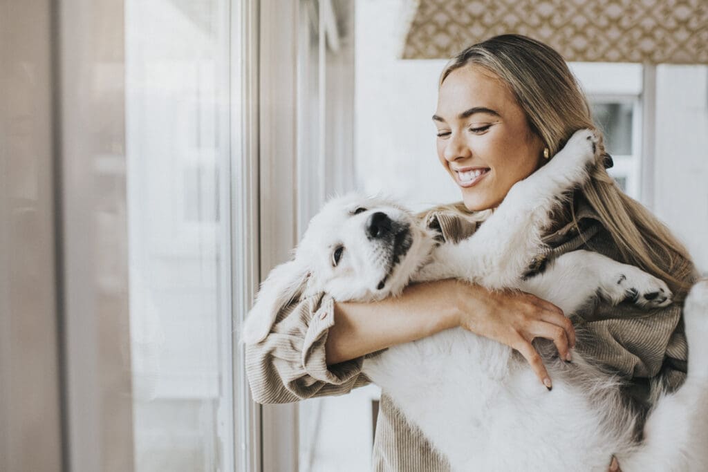 Blonde Frau hält eines ihrer Haustiere - einen weißen Golden Retriever Welpen - im Arm.