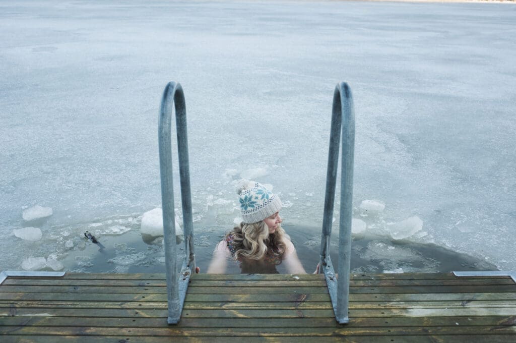 Eine Frau mit Haube und Badeanzug steigt über eine Leiter in eiskaltes Wasser