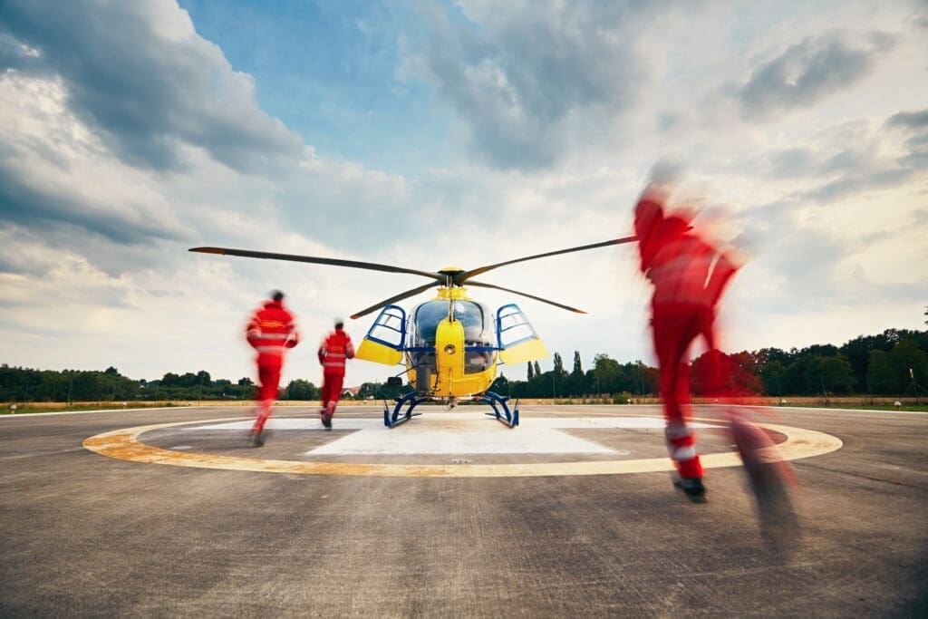 Drei rot gekleidete Notärzte oder Sanitäter laufen zu einem geparkten gelben Hubschrauber
