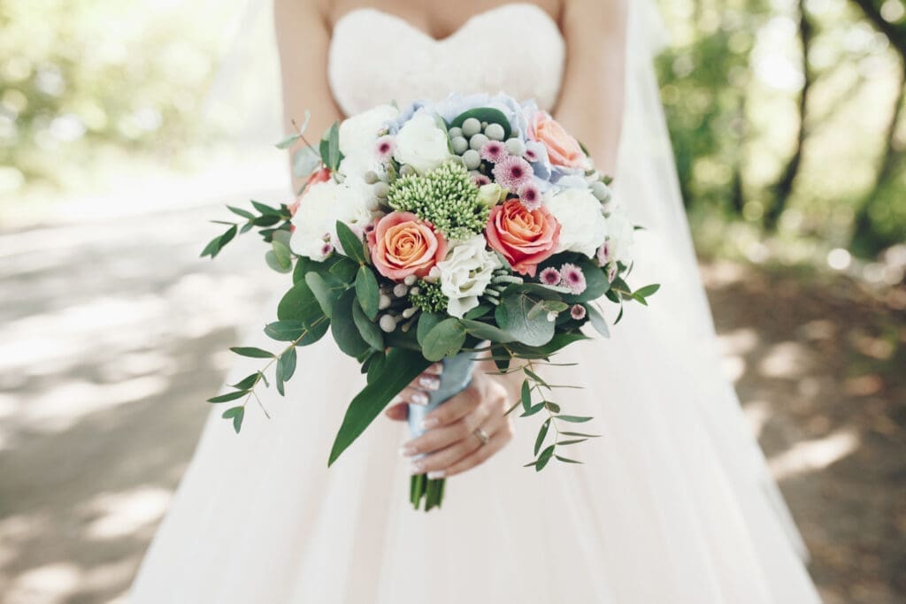 Hochzeitstrends: Heller Blumenstrauß und Brautkleid im Hintergrund.