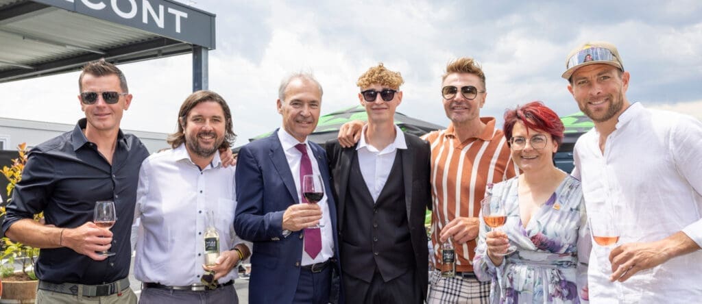 Geschäftsführer Harald Wolfger, Landtagsabgeordneter Hans Unger, Wirtschaftskammer-Präsident Peter Nemeth, Leo Hillinger Junior, Winzer Leo Hillinger, Regionalstellenobfrau Tanja Stöckl und Sonowboard-Olympiasieger Benjamin Karl mit Weingläsern in der Hand vor einem bewölkten Himmel.