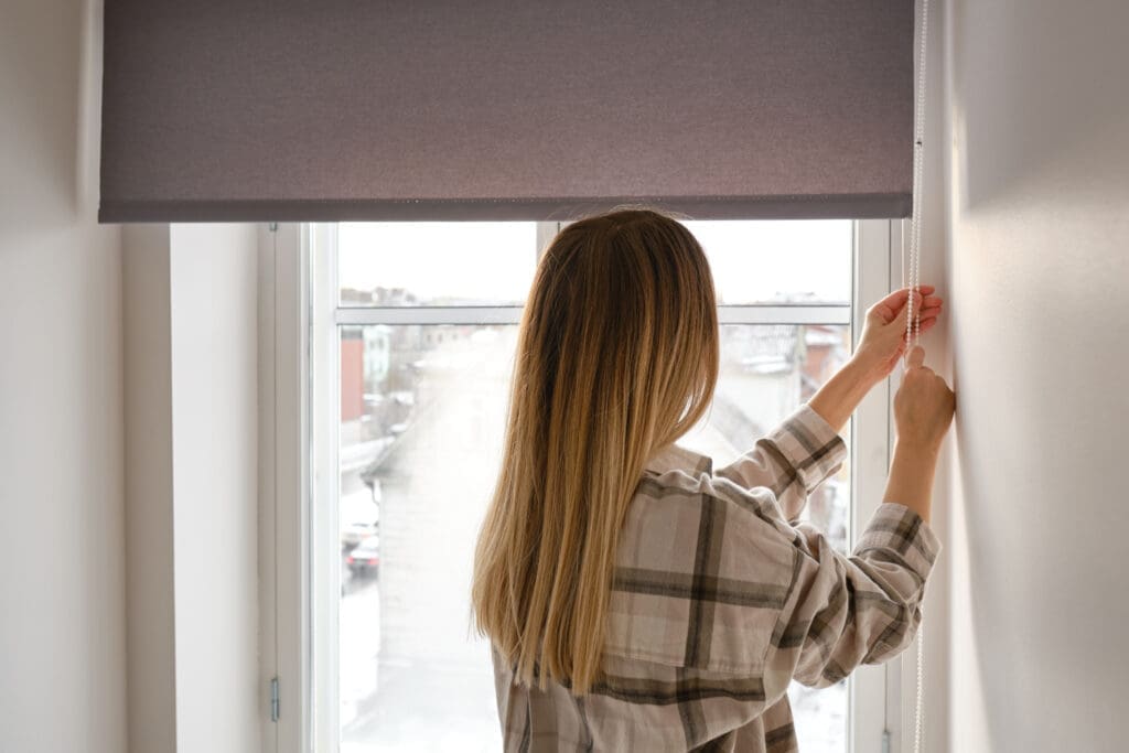 Frau lässt Rollo an ihrem Fenster herunter