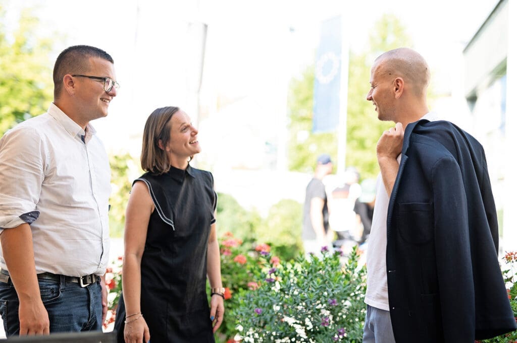 Zwei Mitarbeiter des schau-Teams begrüßen Bürgermeister Maximilian Köllner lächelnd. Er trögt ein weißes Shirt, eine graue Hose und hat ein Sakko lässig über die Schulter geworfen.