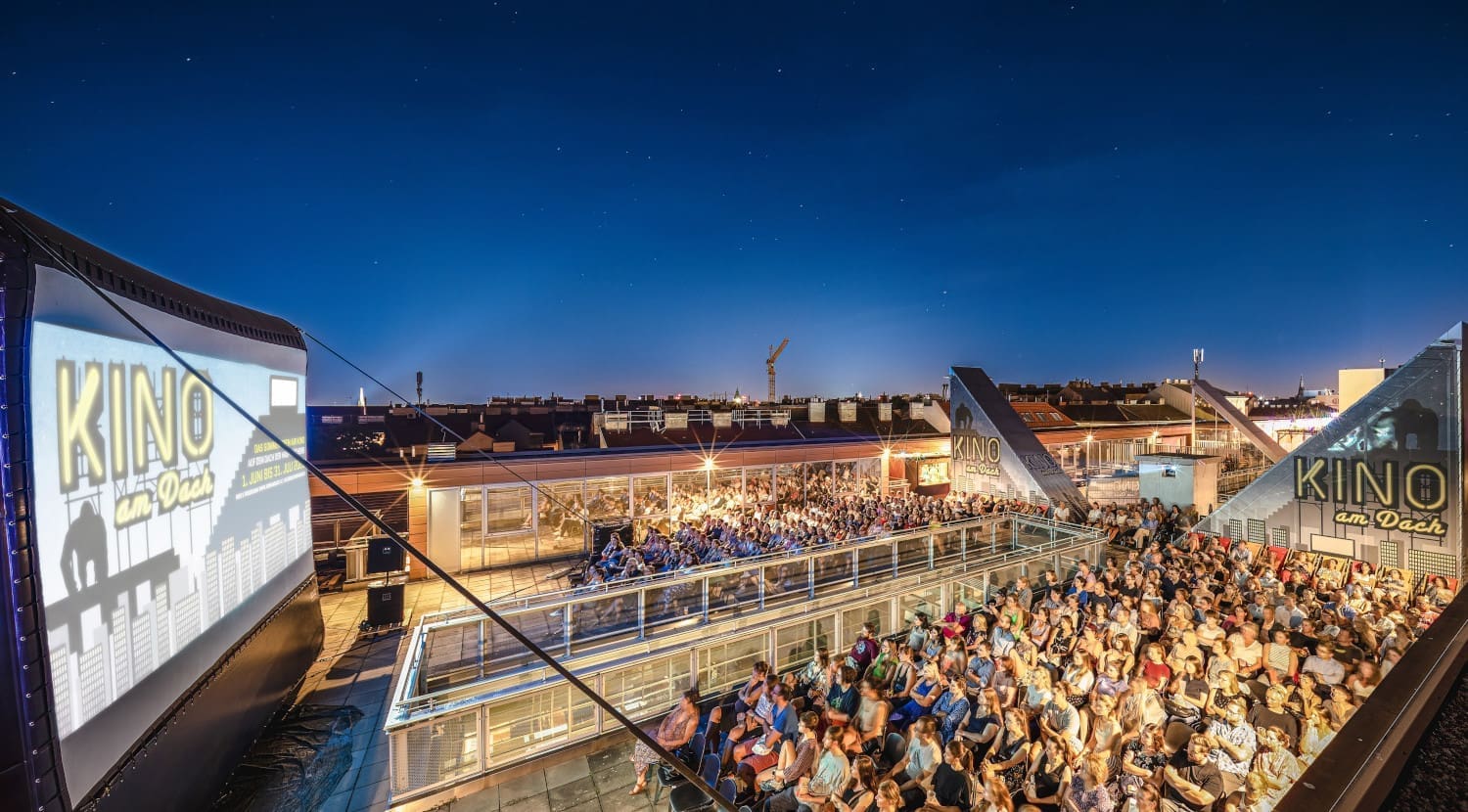 Ein Open-Air-Kino in Wien und Zuschauer sitzen und sehen auf eine Leinwand.