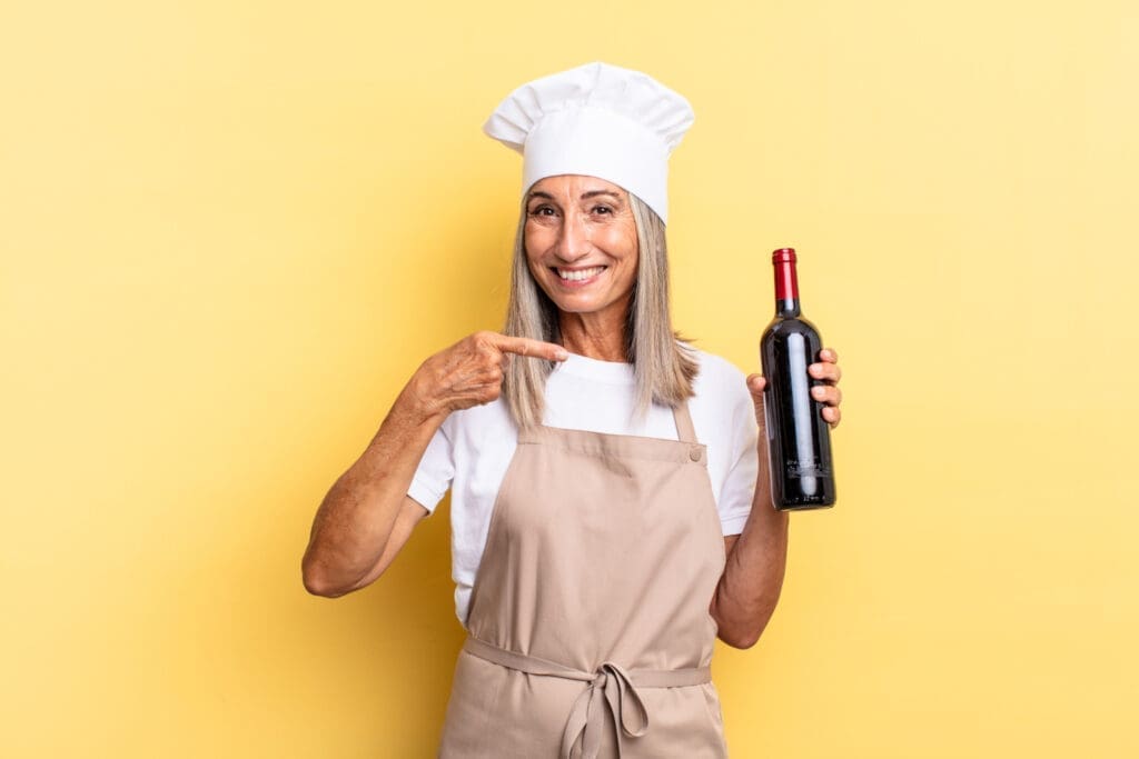 Köchin mit einer Flasche Wein vor gelbem Hintergrund