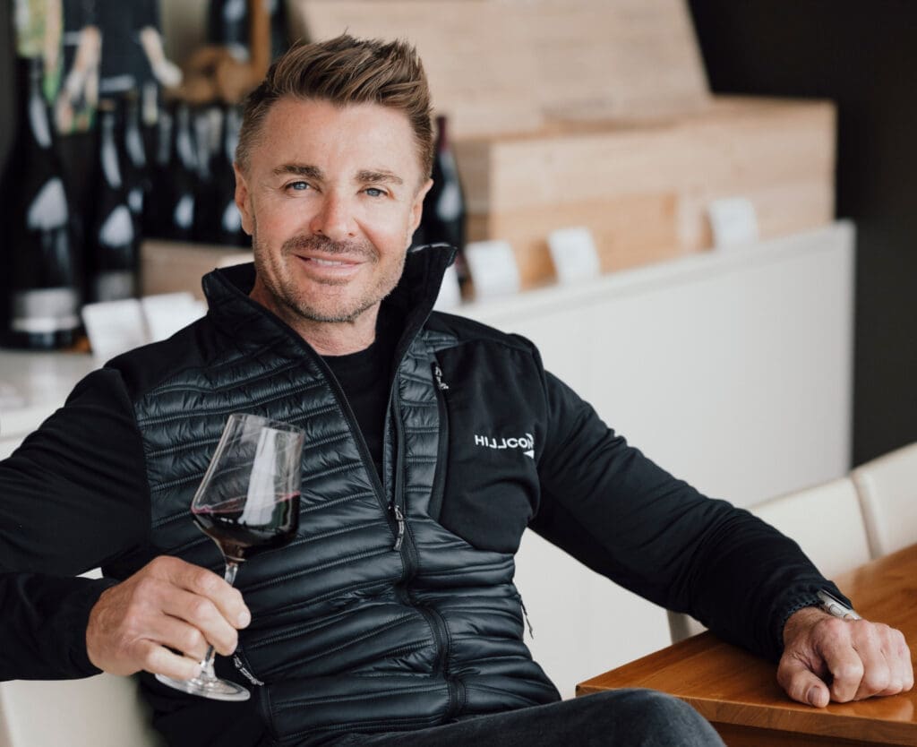 Leo Hillinger sitzt bei einem Tisch mit einem Glas Wein in der Hand