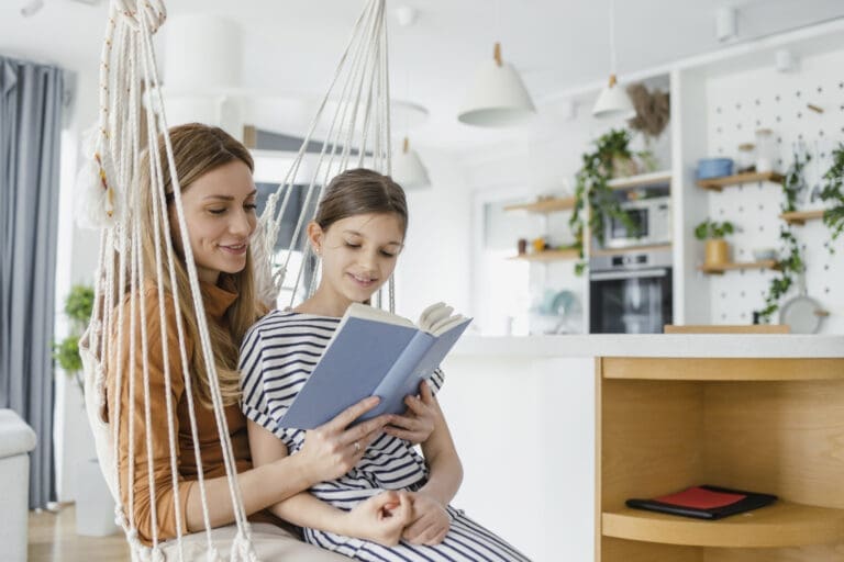 Mutter und Tochter sitzen auf einer Hängematte im Wohnzimmer und sehen sich ein Buch an