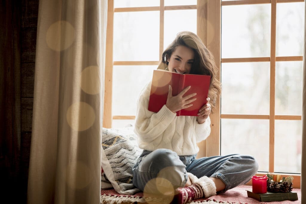 Frau mit Buch in der Hand auf einer Fensterbank