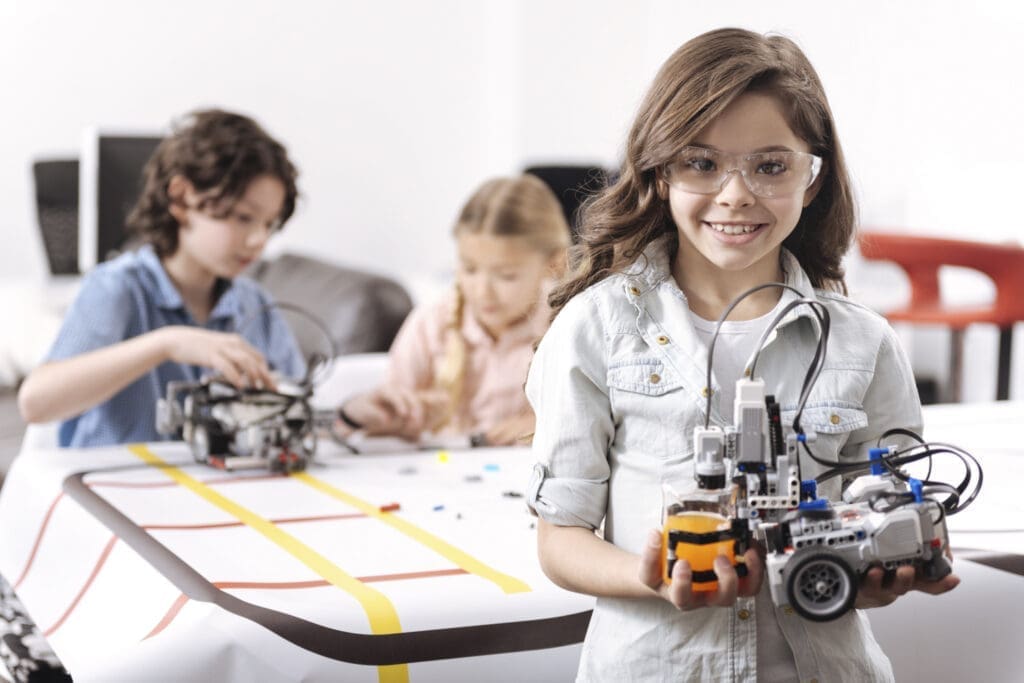 Mädchen mit einem Roboter in der Hand, dahinter zwei weitere Kinder bei der MINT-Ausbildung