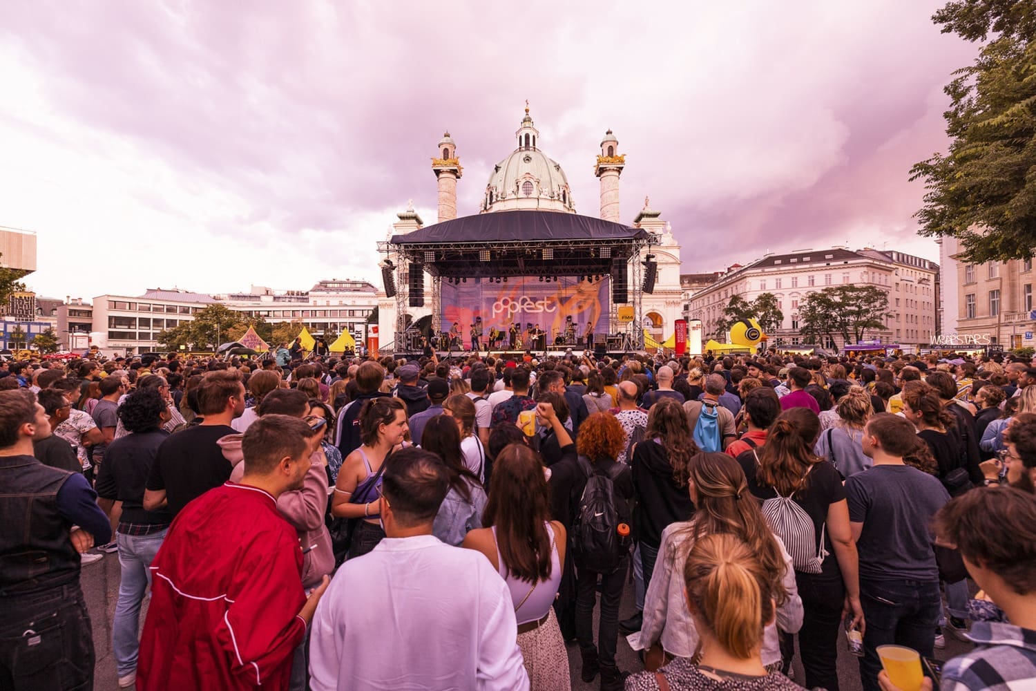 Menschen auf dem Karlsplatz vor einer Bühne. lila Himmel