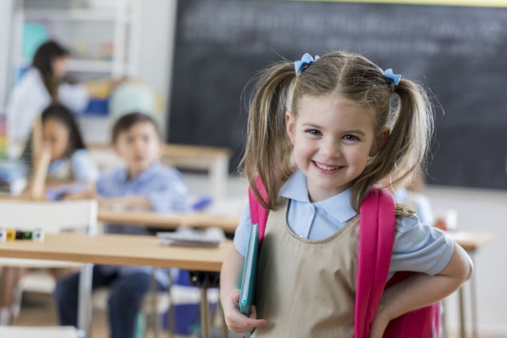 Glückliches Mädchen mit Schultasche beim Schulstart