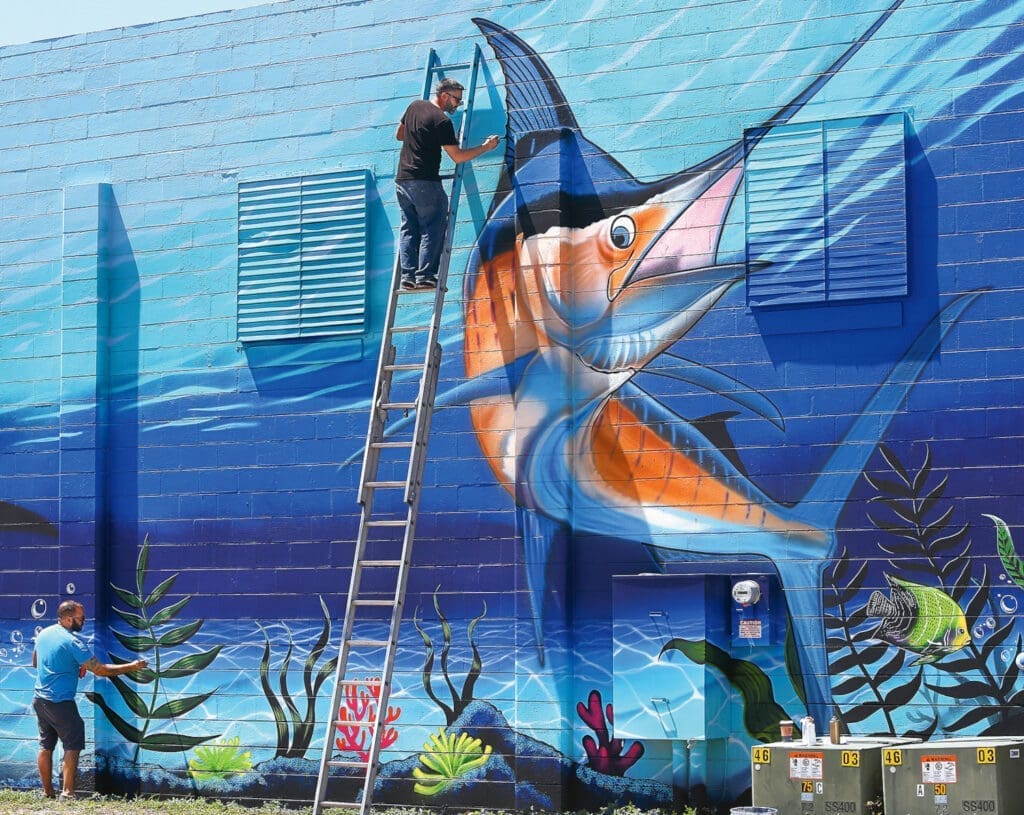 Zwei Männer malen einen Fisch auf eine Wand