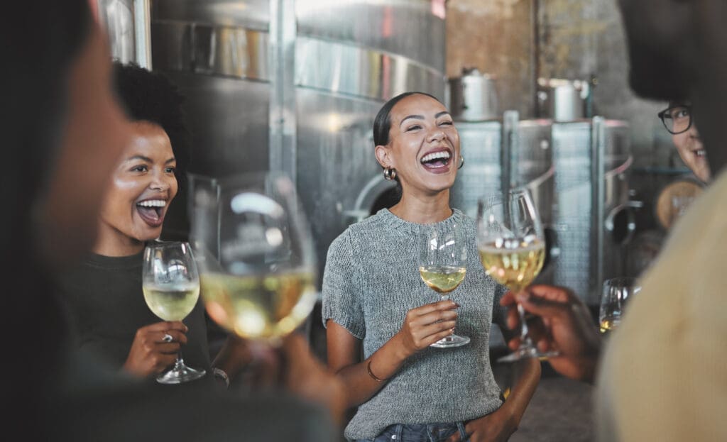 4 Personen mit einem Glas Wein in der Hand am Lachen.