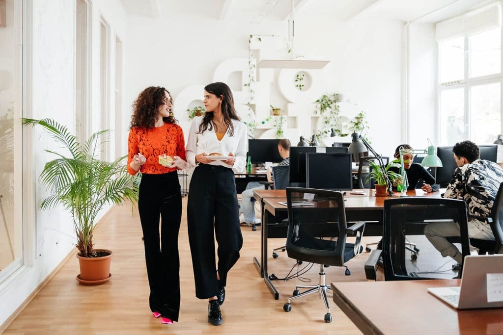 Zwei Frauen gehen in einem Büro an Tischen vorbei