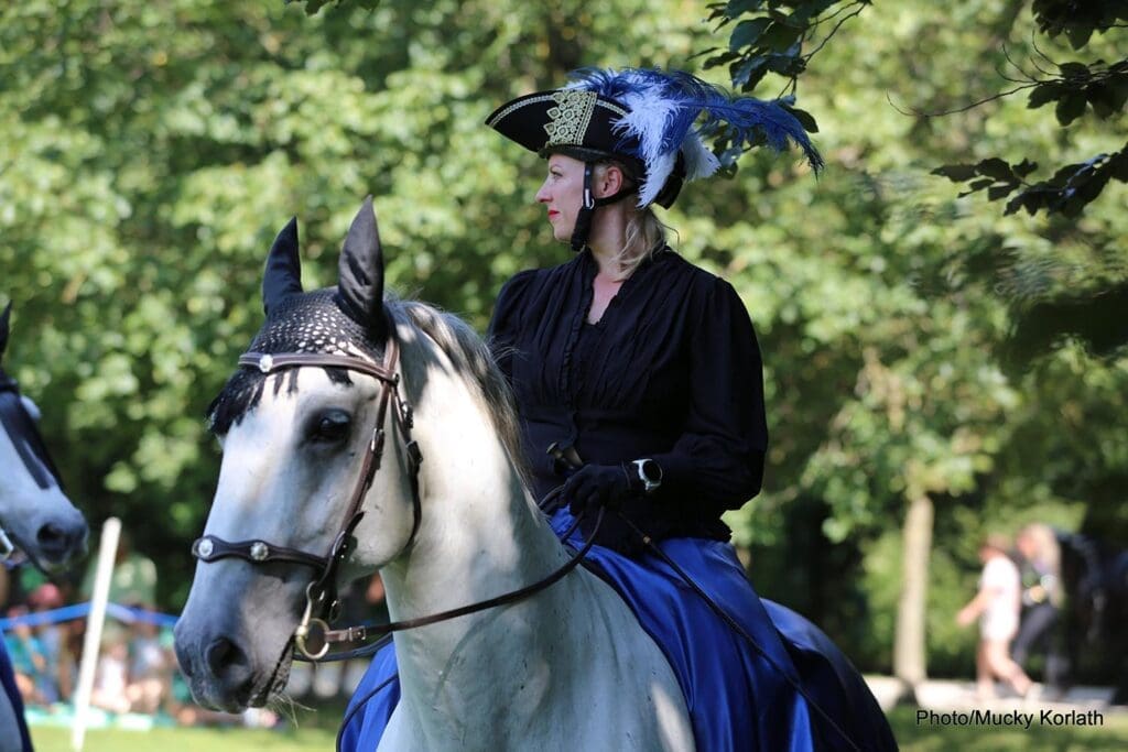 Frau mit Hut und blauen Federn auf Schimmel bei Lipizzaner & Friends.