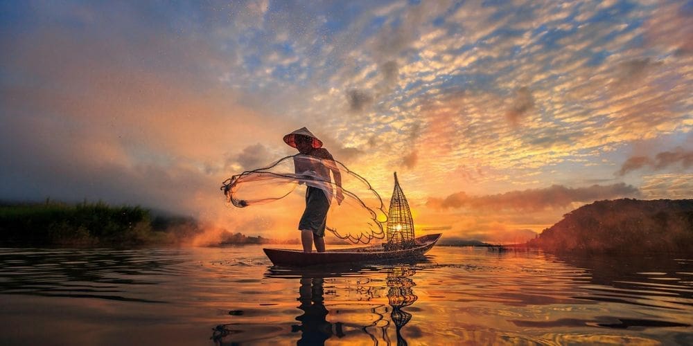 Fischer steht in einem kleinen Boot in der Abenddaämmerung am Mekong