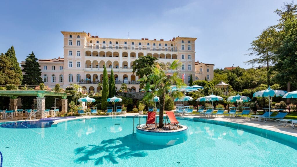 Sommerliche Außenaufnahme des Hotels Kvarner Palace mit Palmeninsel im Outdoorpool