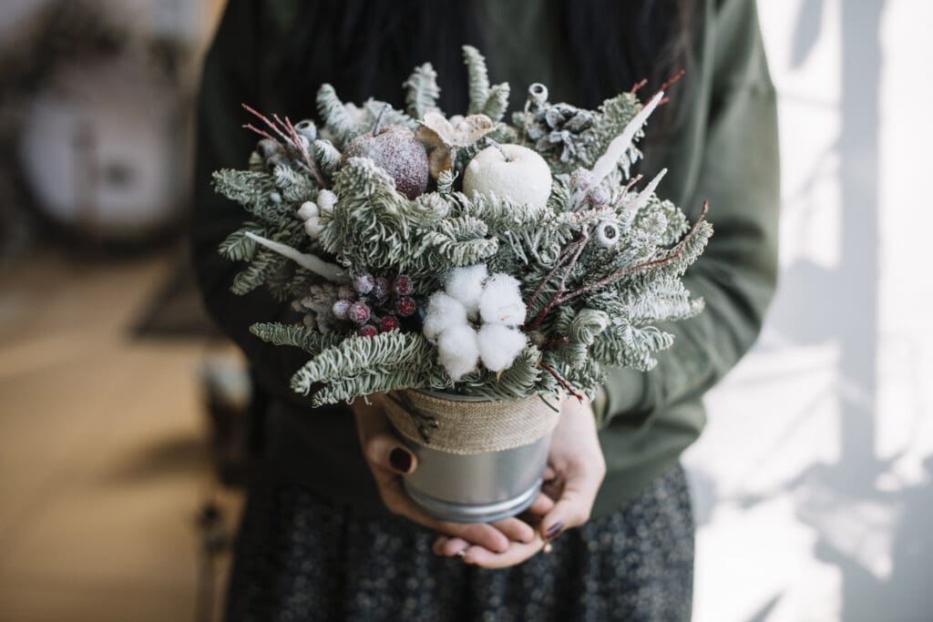 Person mit einem Blumentopf in der Hand. Die Blumen wurden mit Forst-Effekt-Spray besprüht