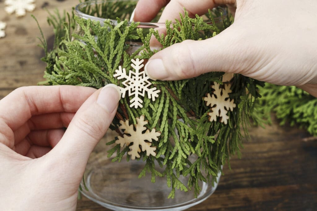 Person bringt Holz-Schneeflocken an einem Einmachglas an