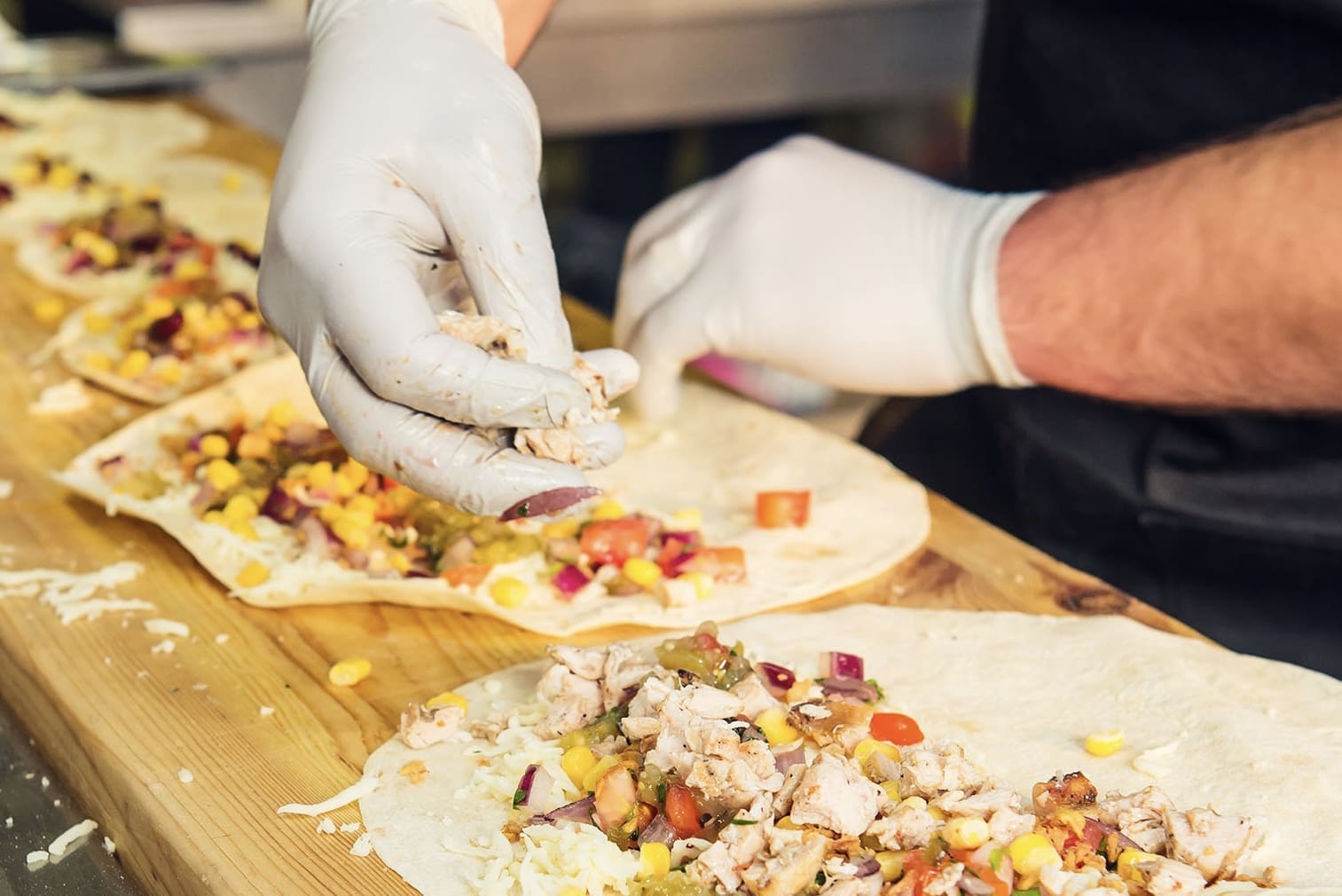 Ein Mensch mit Handschuhen belegt Burritos.
