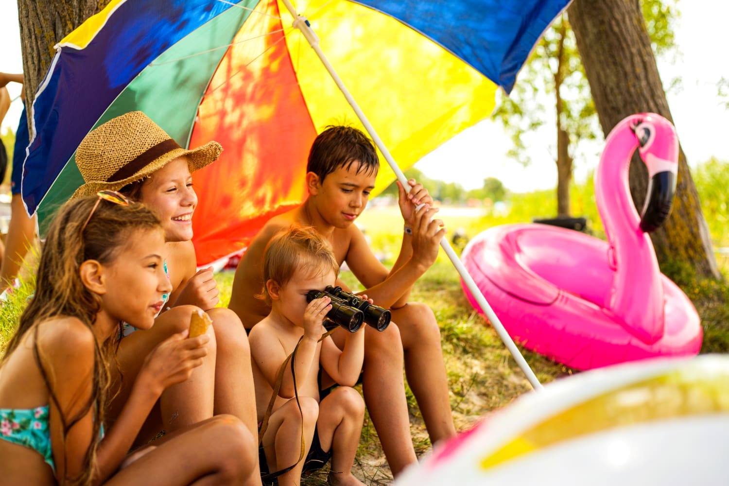 Kinder sitzen unter einem Sonnenschirm und essen ein Eis.