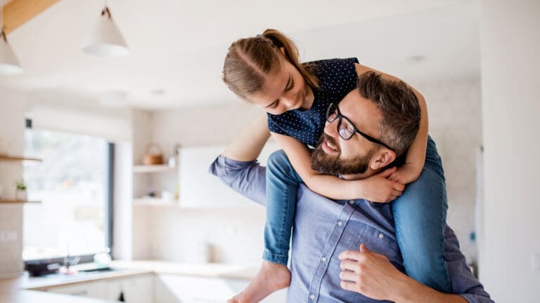Vater trägt Tochter auf den Schultern, im Hintergrund eine weiße Küche