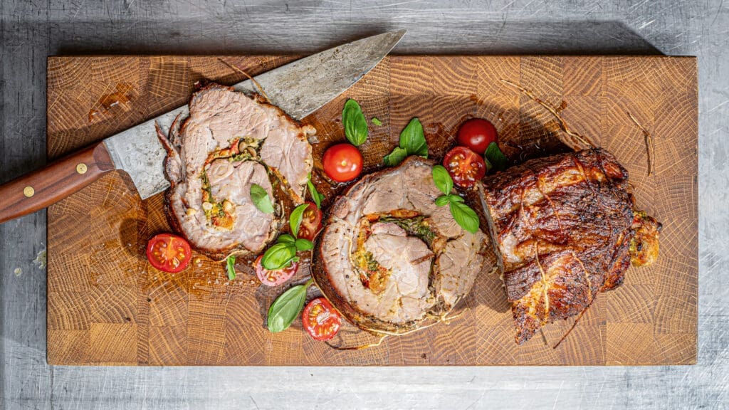 Gefüllter Schweinenacken auf einem Holzbrett, daneben ein Messer