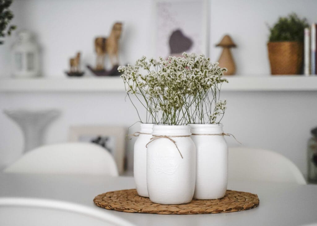 Drei Vasen aus Plastikdosen mit Trockenblumen stehen auf einem Tisch.