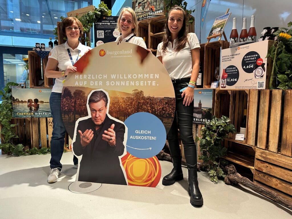 Drei Frauen mit einem Plakat auf einem Messestand