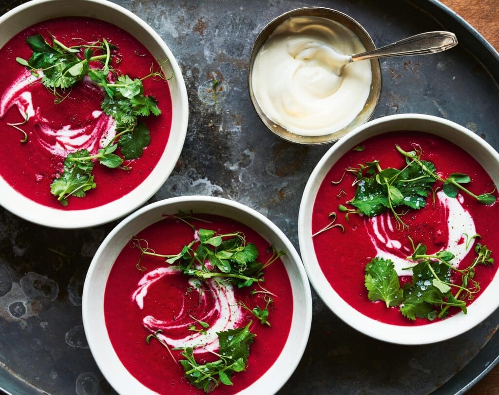 Drei Suppenschalen mit roter Suppe und Kräutern auf Tablett