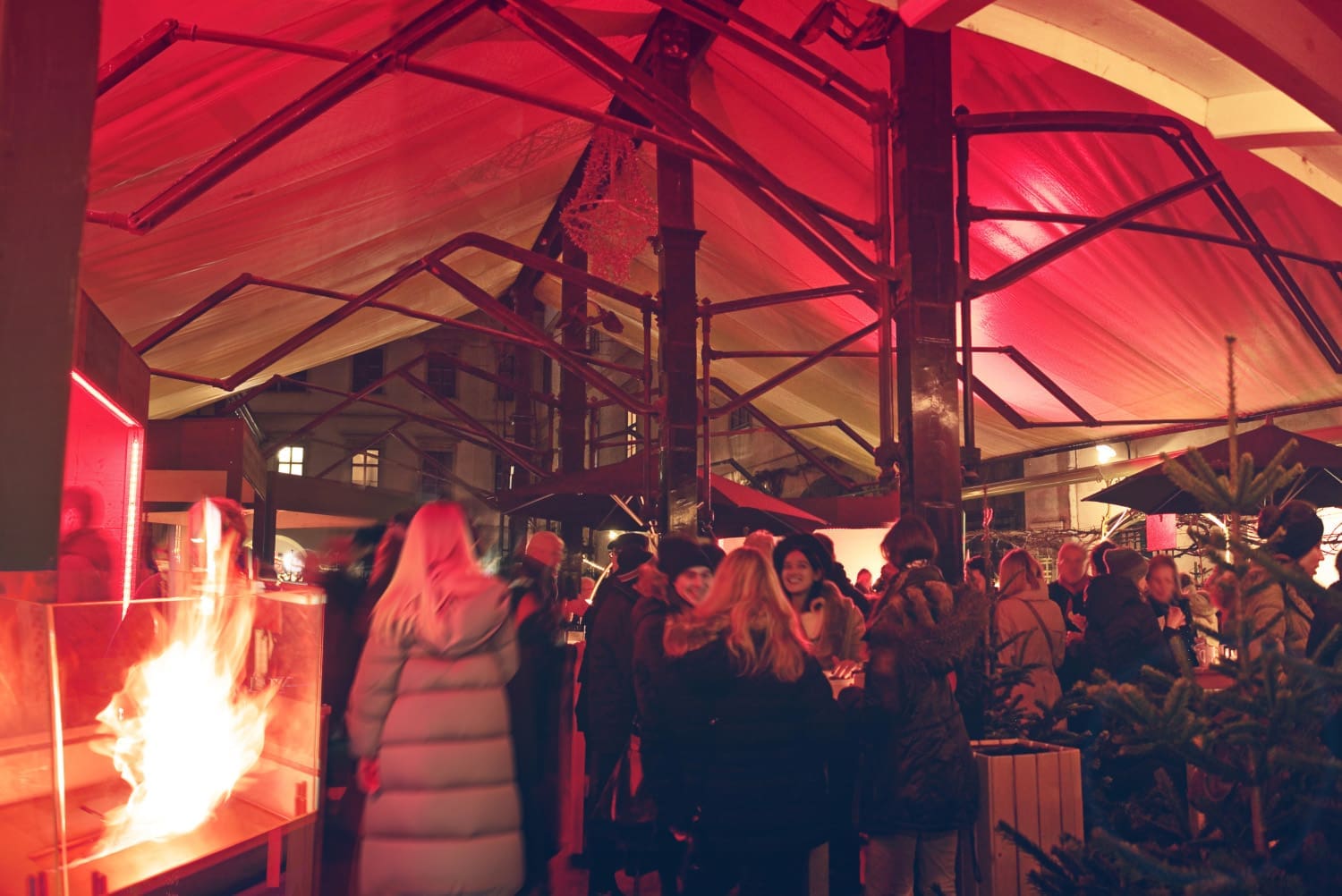 Personen in einem rot-beleuchteten offenen Zelt auf einem Weihnachtsmarkt