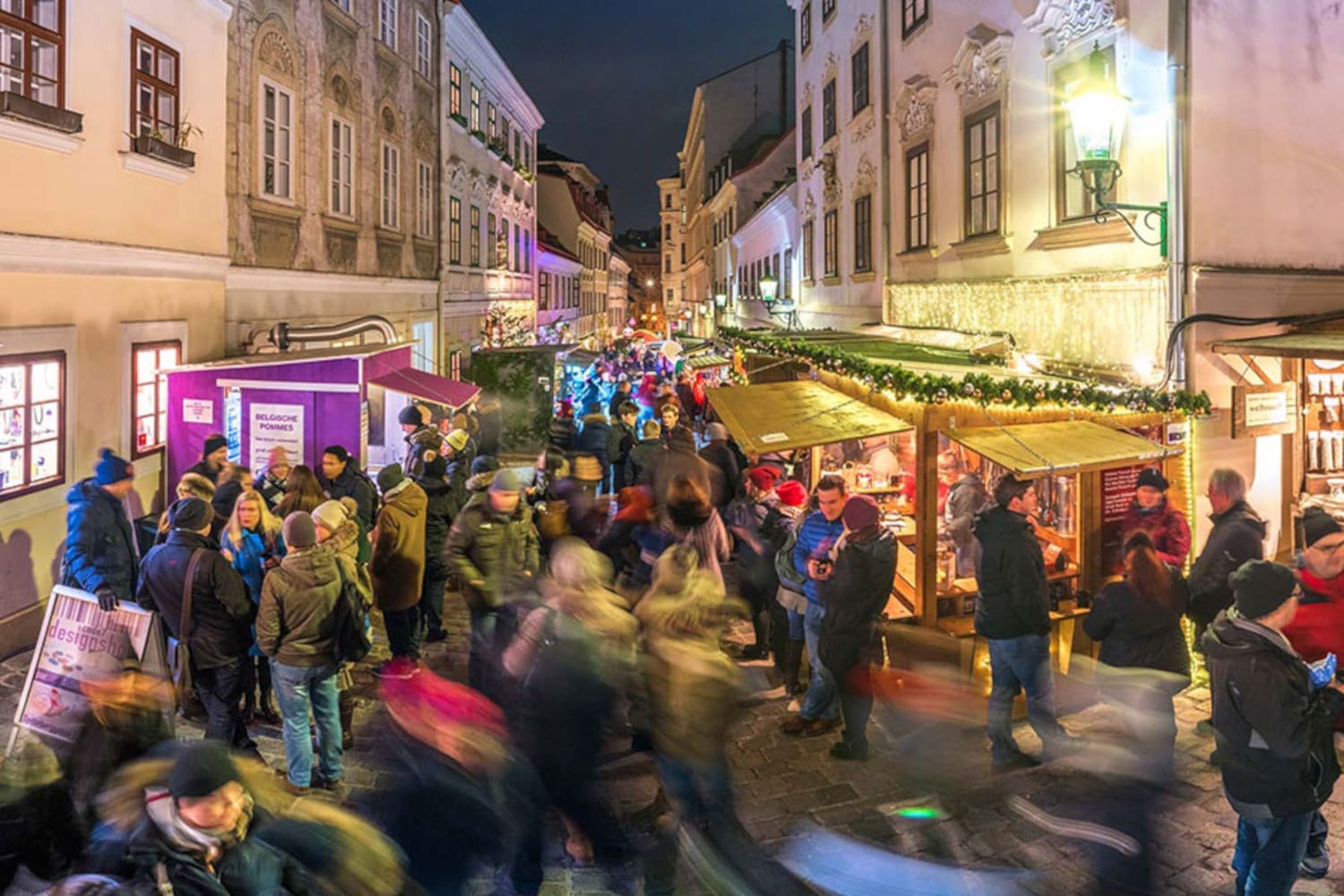 Weihnachtsmarkt entlang einer Gasse, links und rechts an den Gebäudewänden Marktstände, in der Mitte gehen Besucher