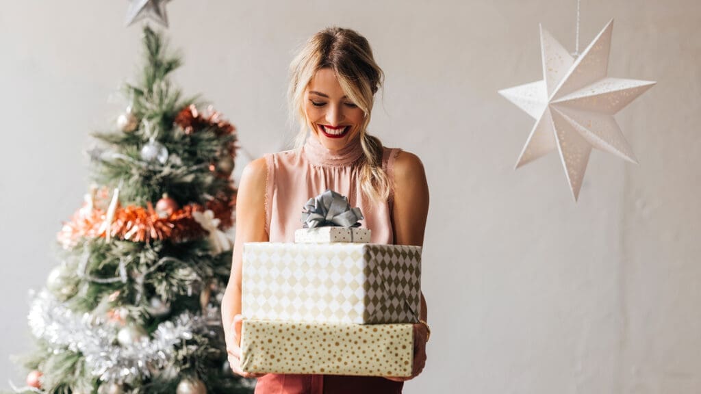 Frau steht vor Christbaum und hält Geschenke in der Hand