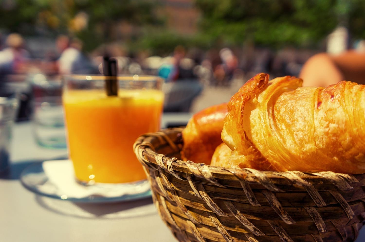Croissant im Korb, dahinter ein Glas Orangensaft