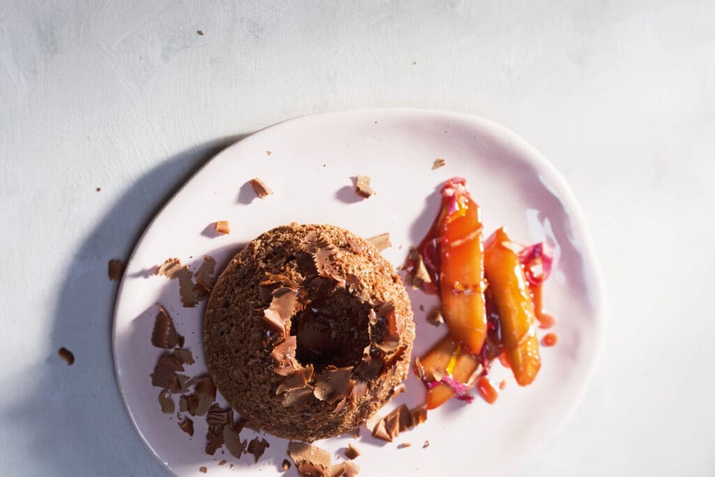 Dunkler Schoko-Soufflékuchen auf weißem Teller mit Rhabarber