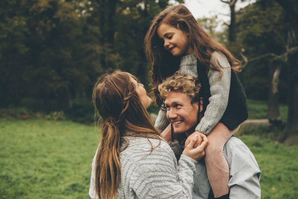 Mutter und Vater mit Kind auf den Schultern im Grünen.