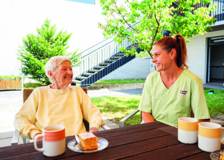 Pflegerin sitzt mit alter Dame bei einem Tisch