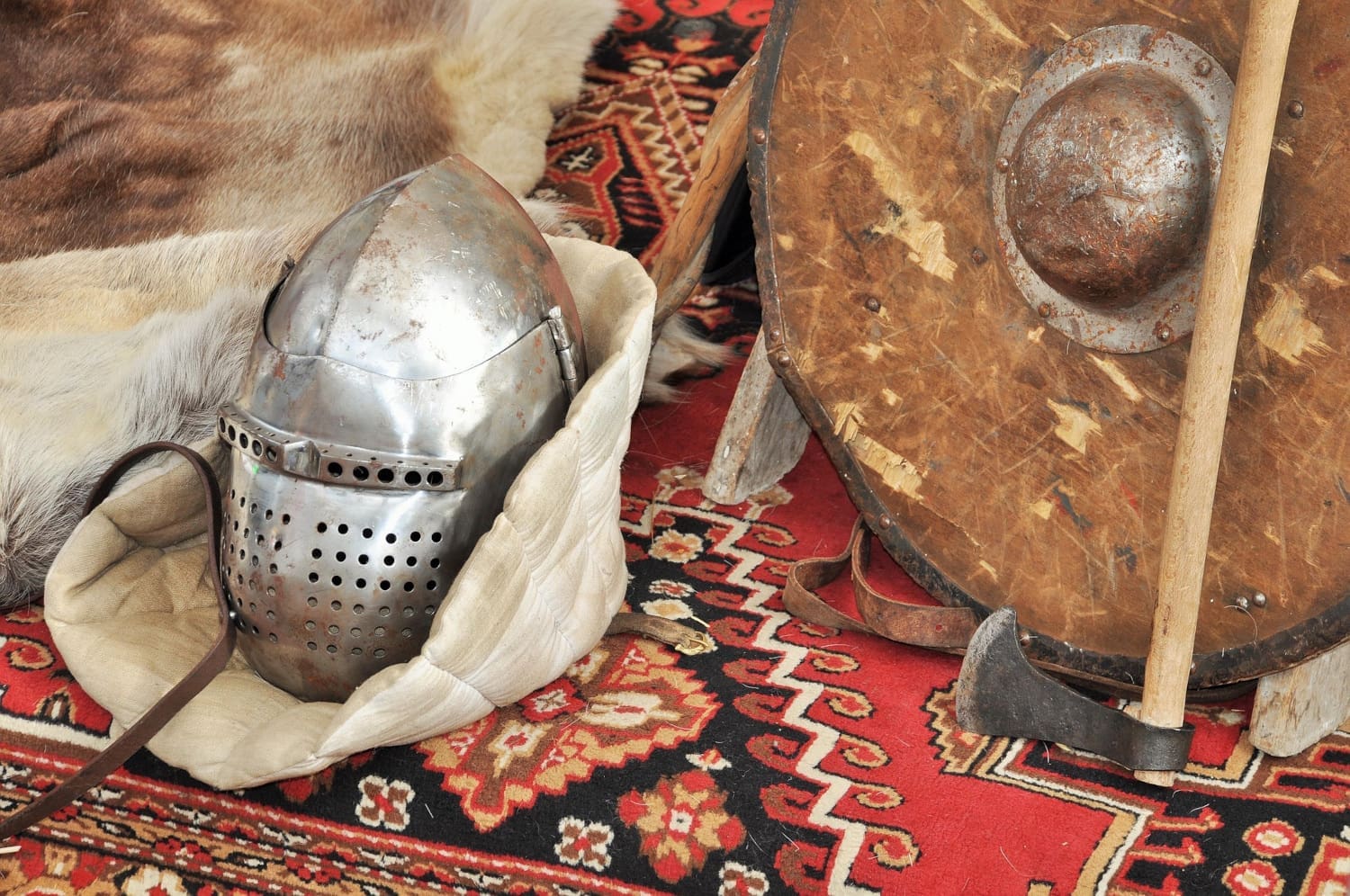 Ritterhelm, Streitaxt und Rundschild auf roter Webdecke