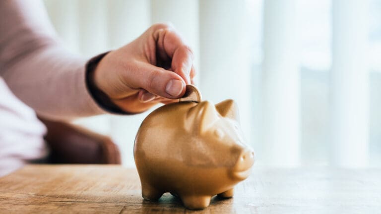 Goldenes Sparschwein und Hand einer Frau mit einem Euro, der in den Schlitz gesteckt wird