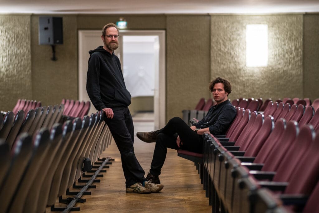 Daniel Meßner und Richard Hemmer in den Sitzreihen eines Theaters