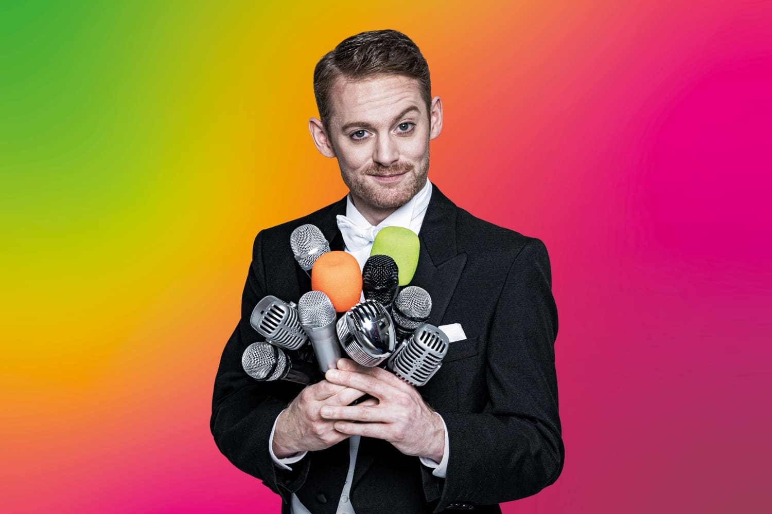 Plakatsujet Bühne Baden, Mann im Anzug mit vielen Mikrophonen vor buntem Hintergrund