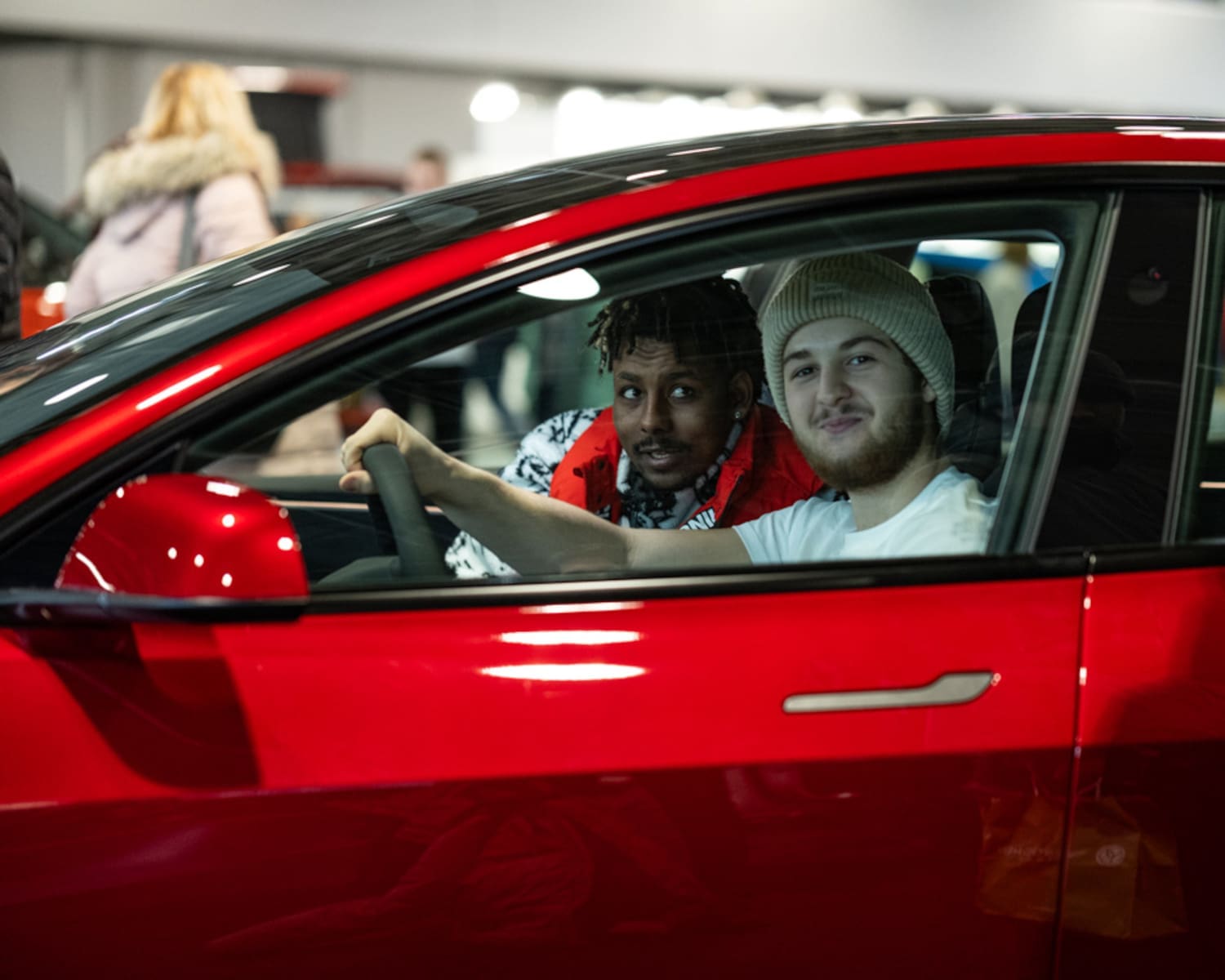 Zwei junge Männer blicken lächelnd aus einem roten Tesla