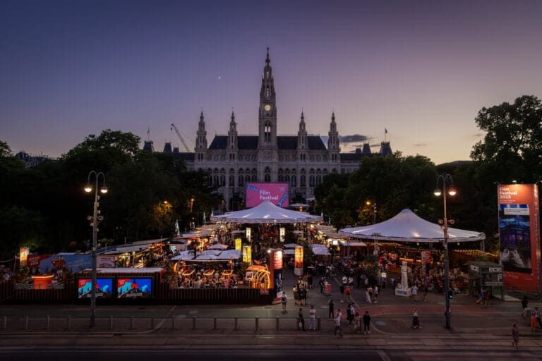 Eröffnungsabend des 35. Filmfestivals auf dem WienerRathausplatz: Blick über die Ringstraße und den Gastronomiebereichmit 28 teilnehmenden Betrieben auf die imposante Filmleinwand unddas festlich beleuchtete Rathaus kurz vor Filmbeginn.